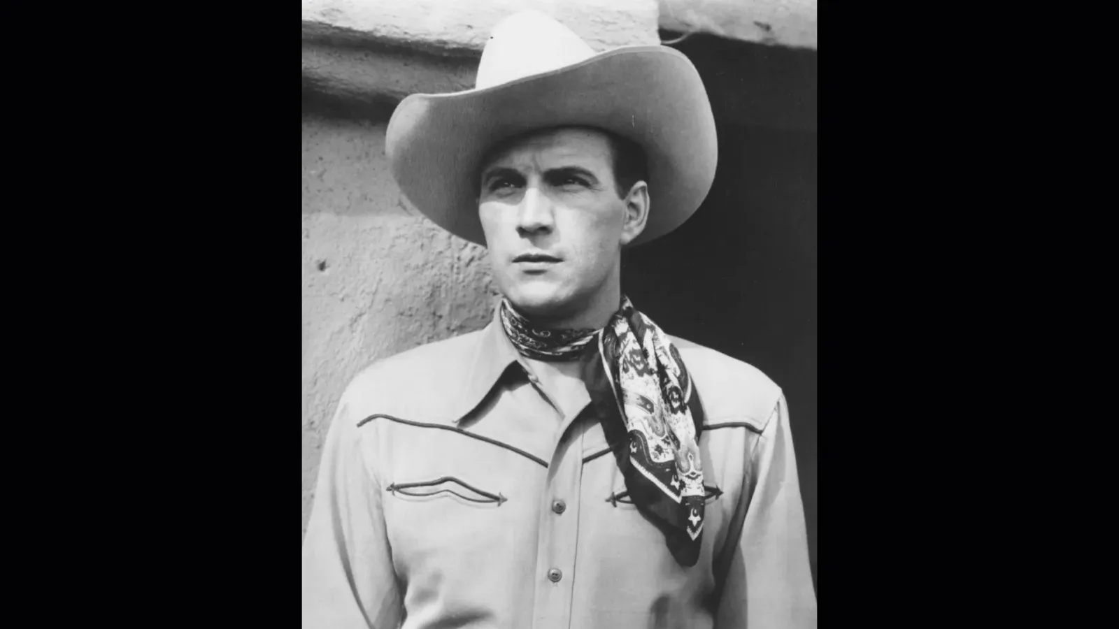 Black‑and‑white portrait of Tom Tyler wearing a wide‑brim cowboy hat and patterned neckerchief, looking off camera with a strong leading‑man stare.